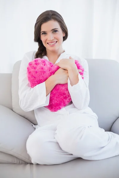 Pleased woman in white pajamas cuddling a heart shaped pillow — Stock Photo, Image