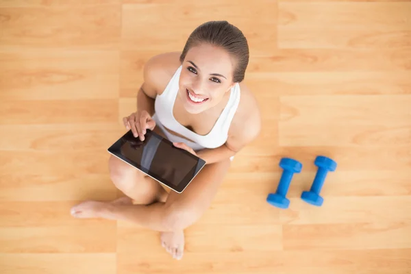 Sporty brunette using a tablet and sitting next to dumbbells — Stock Photo, Image