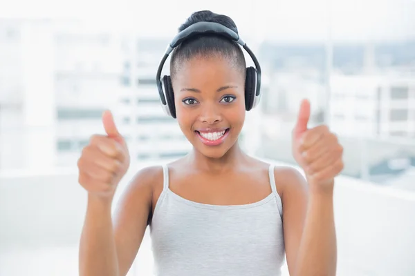 Mujer sonriente escuchando música con auriculares y dando pulgares hacia arriba —  Fotos de Stock