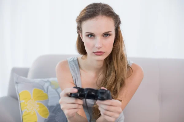 Mujer joven y seria sentada en un sofá jugando videojuegos — Foto de Stock