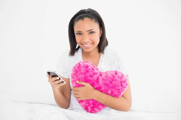 Delighted young model holding a pillow and a mobile phone — Stock Photo, Image