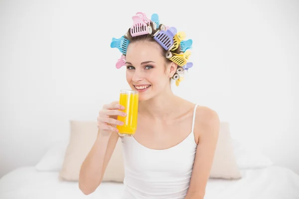 Cute woman in hair curlers drinking orange juice — Stock Photo, Image