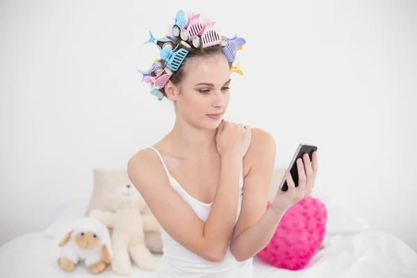 Stern mulher em encrespadores de cabelo olhando para o seu telefone móvel — Fotografia de Stock