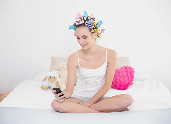 Pleased woman in hair curlers using her mobile phone — Stock Photo, Image