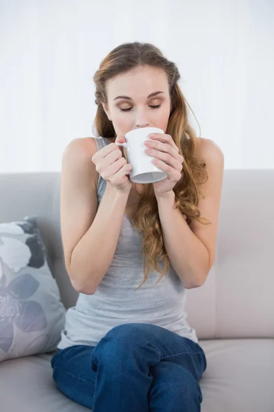 Ung kvinna sitter på soffan dricka från mugg — Stockfoto