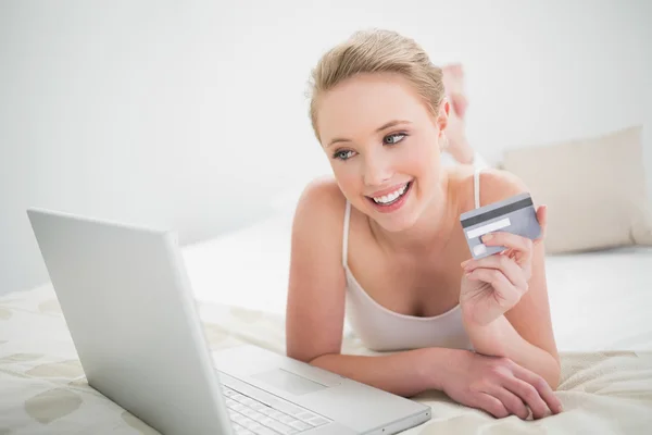 Natural rubia sonriente celebración de la tarjeta de crédito y mirando el ordenador portátil — Foto de Stock