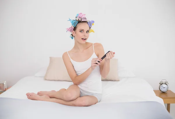 Surprised woman in hair curlers filing her nails — Stock Photo, Image