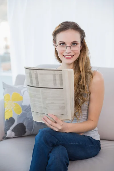 Vidám fiatal nő ül a kanapén holding újság — Stock Fotó