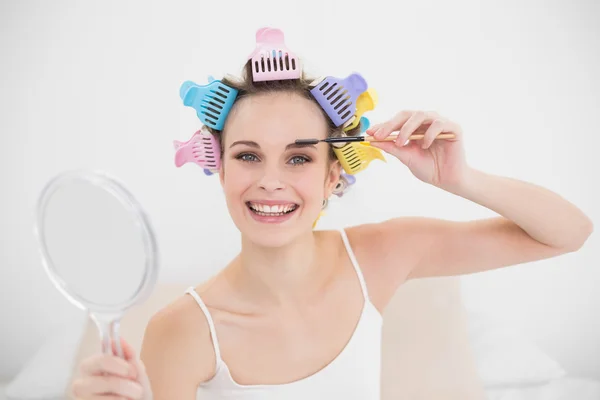 Happy woman in hair curlers brushing her eyebrows — Stock Photo, Image