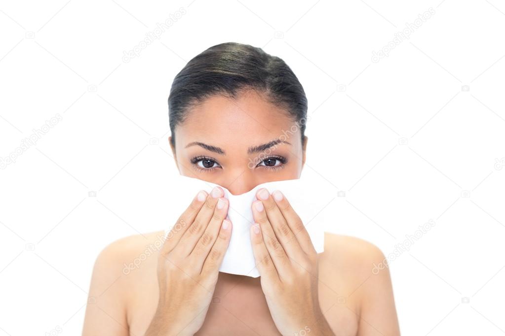 Sad young woman sneezing in a tissue