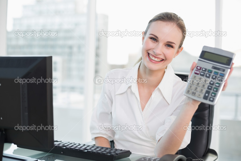 Happy businesswoman showing calculator sitting at desk