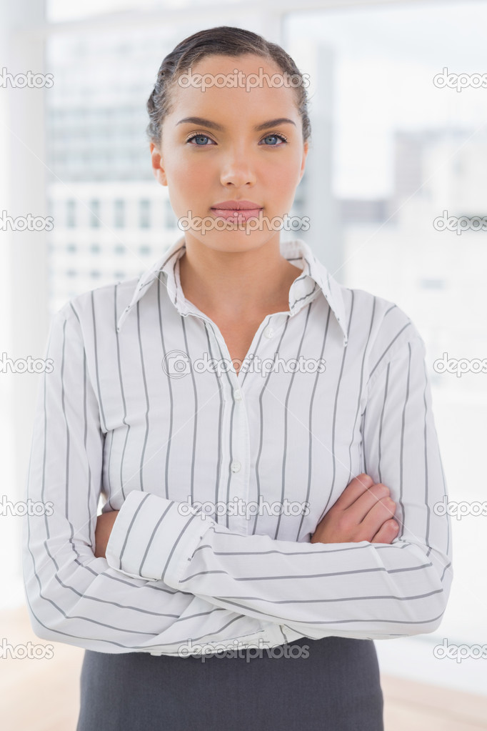 Serious businesswoman standing in an office crossing arms
