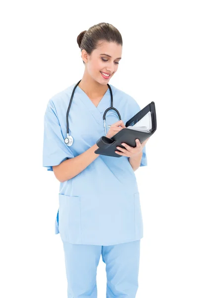 Attractive nurse in blue scrubs filling an agenda — Stock Photo, Image