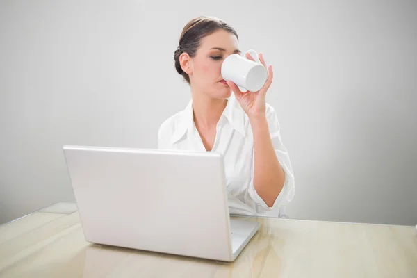 Серьезная деловая женщина, работающая на ноутбуке, пьет кофе — стоковое фото