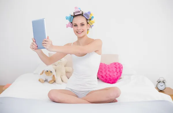 Mujer alegre en rulos de pelo tomando una foto de sí misma con una tableta — Foto de Stock