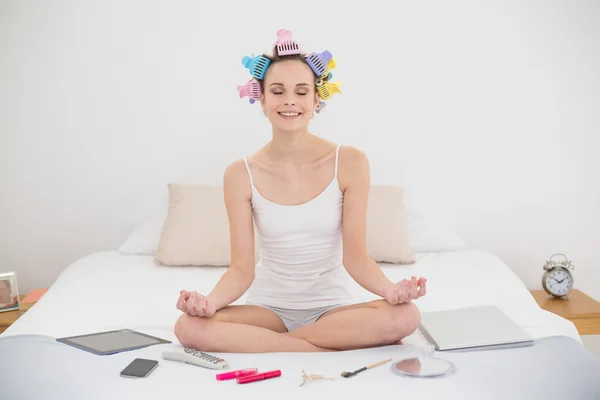 Donna rilassata in bigodini per capelli meditando in posizione di loto — Foto Stock