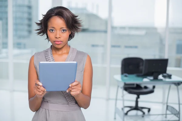 Mujer de negocios seria de pie en su oficina sosteniendo la tableta — Foto de Stock