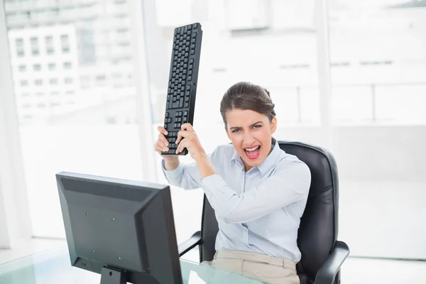 Раздраженная деловая женщина бросает клавиатуру на свой компьютер — стоковое фото