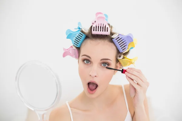Woman in hair curlers opening her mouth while applying mascara — Stock Photo, Image