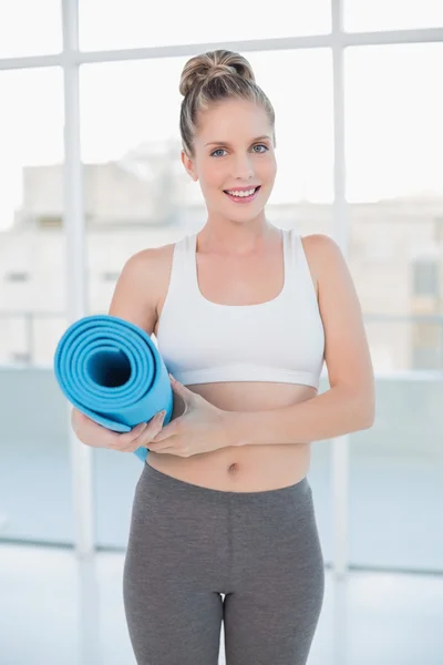 Sonriente rubia deportiva sosteniendo tapete de ejercicio balanceado —  Fotos de Stock