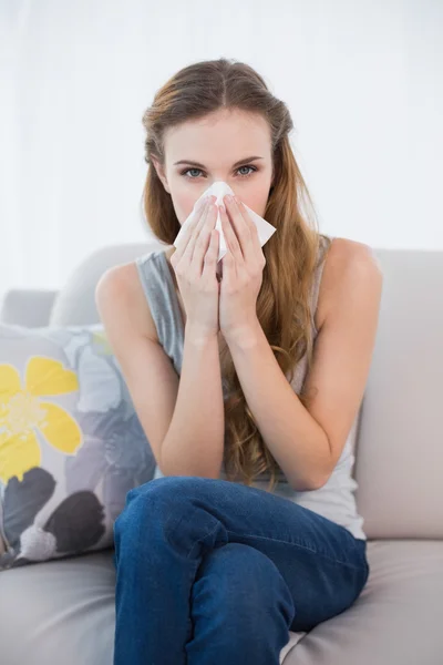 Sick woman sitting on sofa blowing her nose — Stock Photo, Image