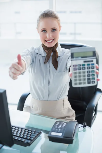 Blonde smiling businesswoman showing calculator and thumb up — Stock Photo, Image