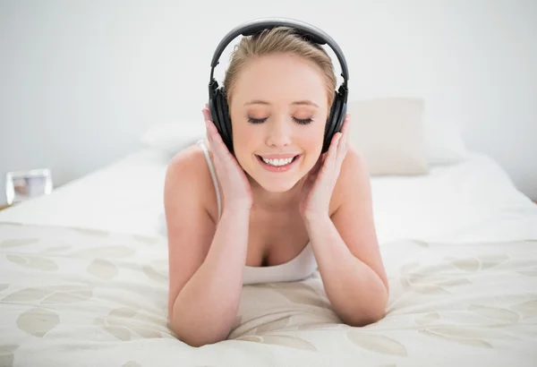 Doğal mutlu sarışın yatakta yatarken ve kapalı gözler ile müzik dinlemek — Stok fotoğraf
