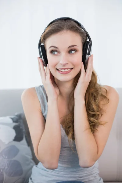 Uśmiechnięta młoda kobieta siedzi na kanapie, słuchanie muzyki — Zdjęcie stockowe