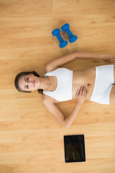 Sportieve brunette liggen naast een Tablet PC- en halters — Stockfoto