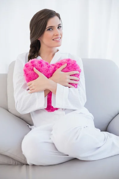 Mujer pacífica en pijama blanco abrazando una almohada en forma de corazón — Foto de Stock