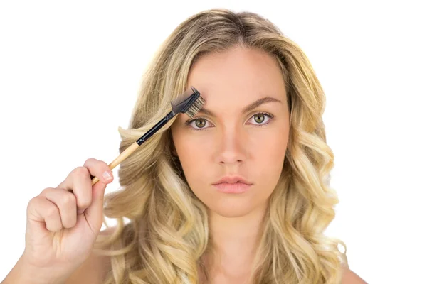 Serious curly haired blonde using eyebrow brush — Stock Photo, Image