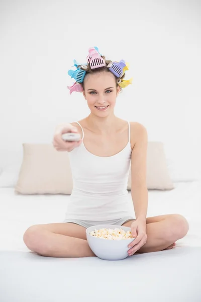 Concentrated woman in hair curlers watching tv while eating popcorn — Stock Photo, Image