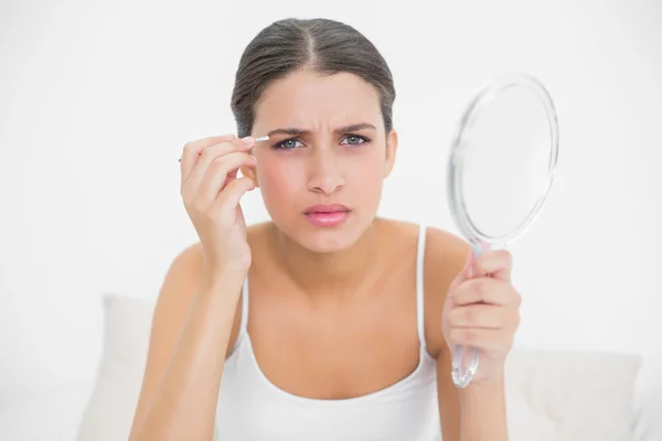 Model in white pajamas plucking her eyebrows — Stock Photo, Image