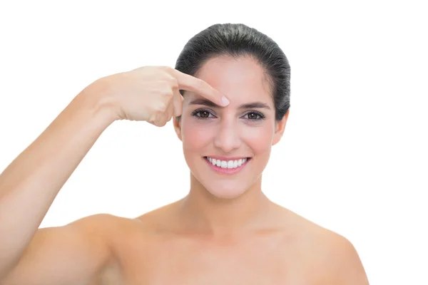 Smiling bare brunette pointing at her face — Stock Photo, Image