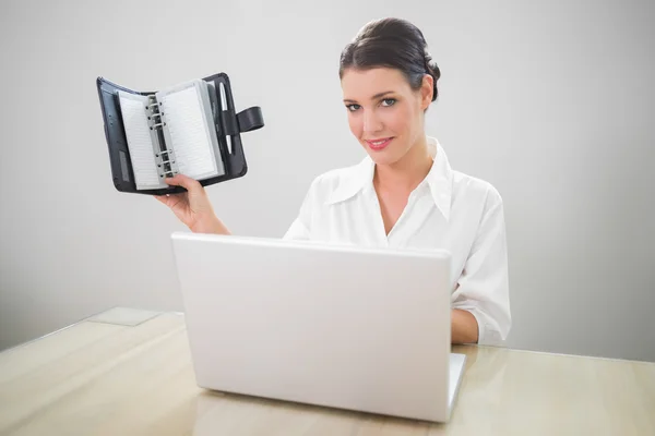 Smiling businesswoman working on laptop holding datebook — Stock Photo, Image