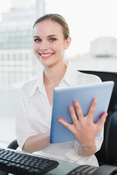Uśmiechnięta kobieta siedzi przy biurku, trzymając tablet pc — Zdjęcie stockowe