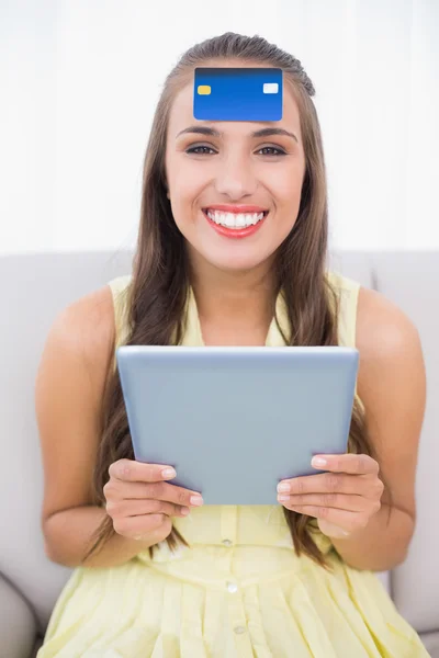 Happy brunette with credit card on forehead holding tablet — Stock Photo, Image