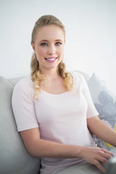 Casual cheerful blonde sitting on couch using laptop — Stock Photo, Image