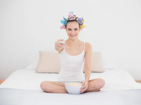 Cute woman in hair curlers watching tv while eating popcorn — Stock Photo, Image