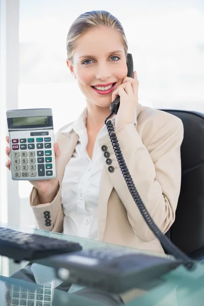 Femme d'affaires blonde souriante au téléphone montrant calculatrice — Photo