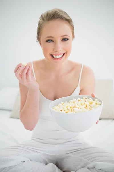 Natural cheerful blonde holding bowl of popcorn on bed — Stock Photo, Image