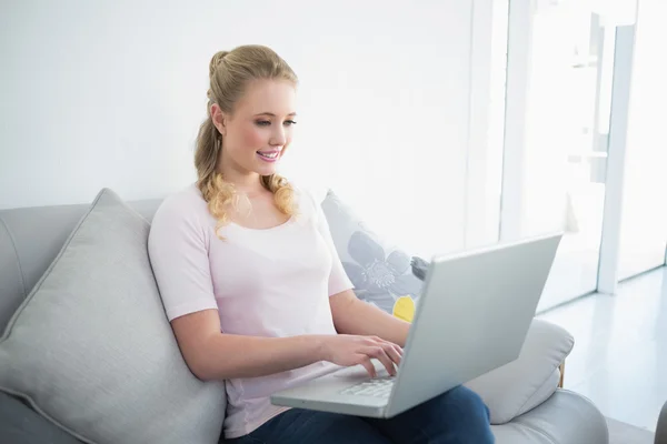 Casual content blonde sitting on couch using laptop — Stock Photo, Image