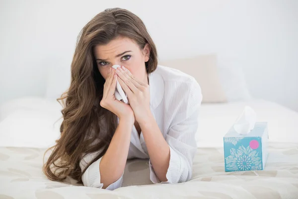 Frowning woman in white pajamas sneezing in a tissue — Stock Photo, Image