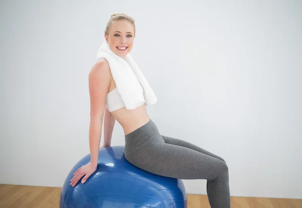 Lachende sportieve blonde met handdoek rond haar nek zittend op oefening bal — Stockfoto