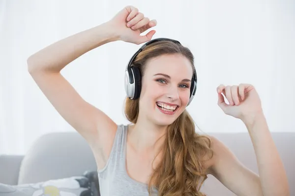 Dancing young woman sitting on sofa listening to music — Stock Photo, Image