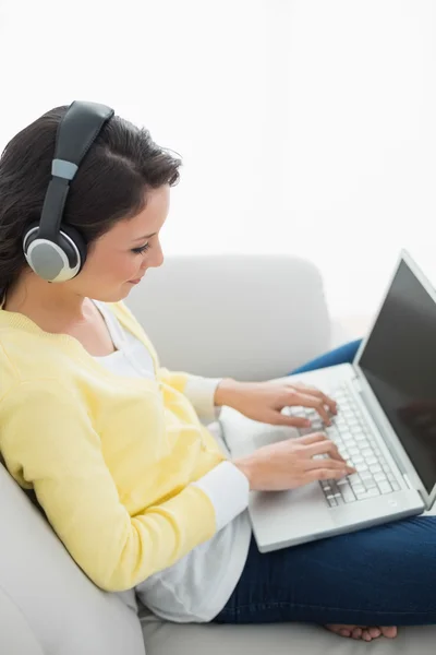 Calma morena casual en cárdigan amarillo escuchando música mientras usa un portátil —  Fotos de Stock