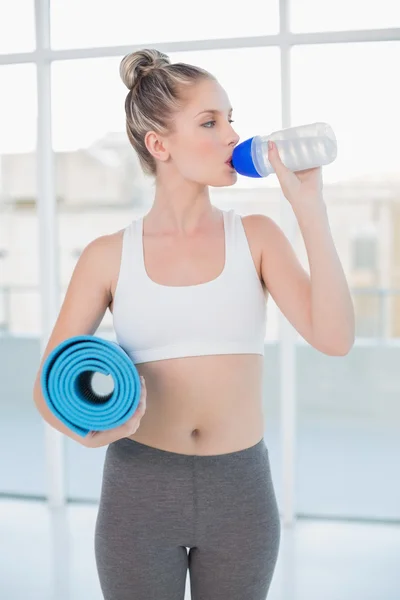 Sporty loira beber água segurando tapete de exercício — Fotografia de Stock