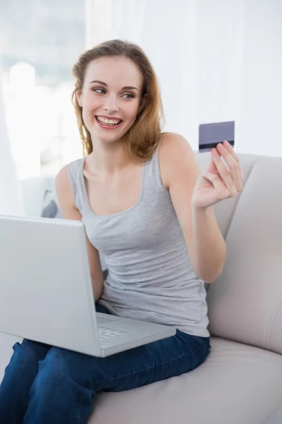 Rindo jovem mulher sentada no sofá usando laptop — Fotografia de Stock