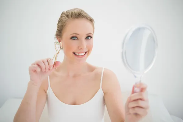 Natural smiling blonde holding mirror and eyelash curler — Stock Photo, Image