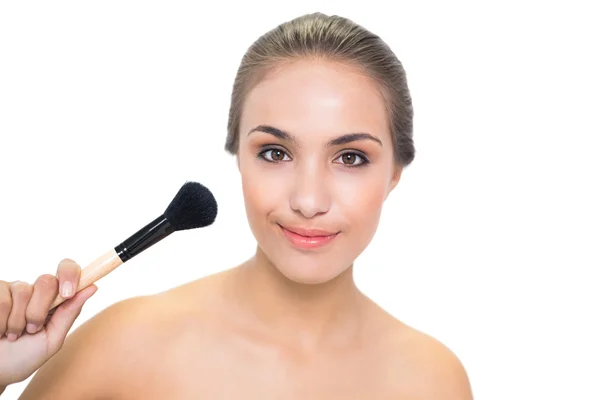 Smiling young woman pointing a powder brush to her face — Stock Photo, Image